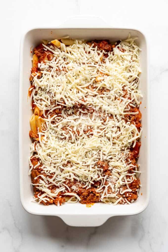 Sprinkled Parmesan and mozzarella cheese in a casserole dish over meat sauce and pasta.