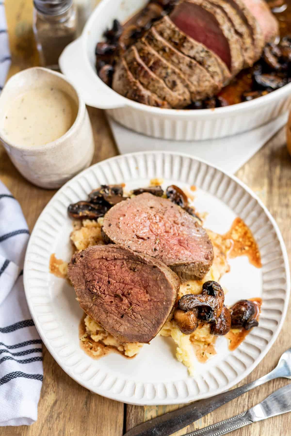 Two slices of beef tenderloin on a plate with mashed potatoes and mushrooms.