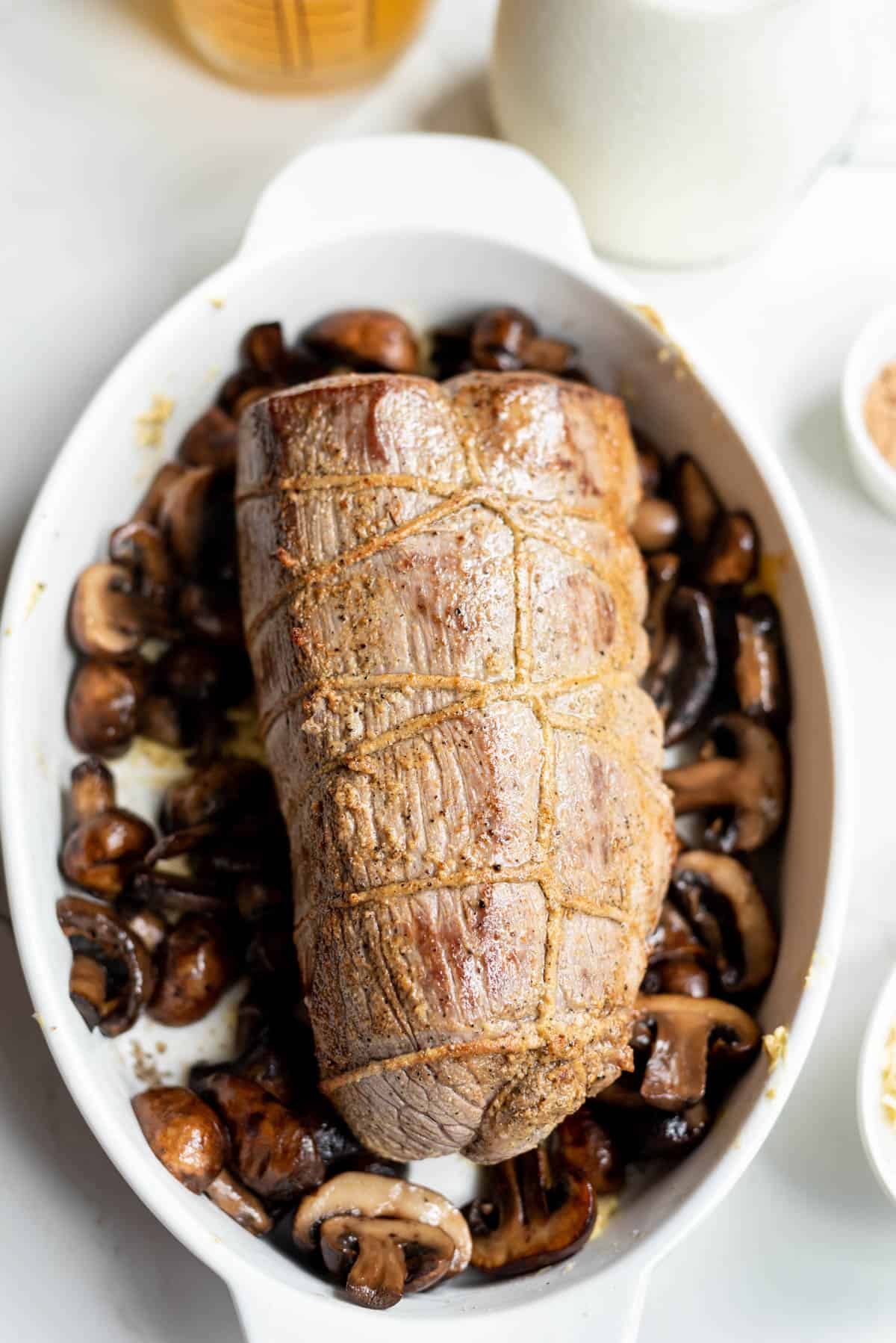 A seared beef tenderloin roast in a roasting pan with mushrooms.