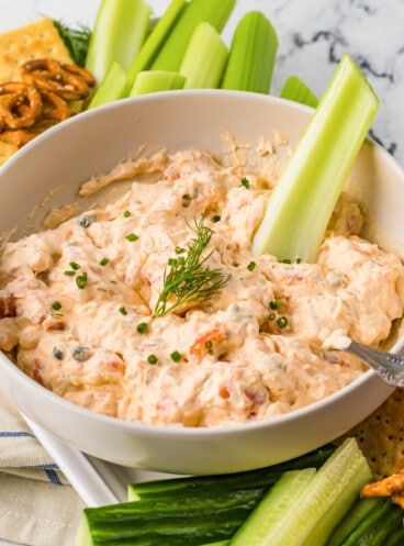 Smoked salmon dip in a white bowl with a stick of celery in it.