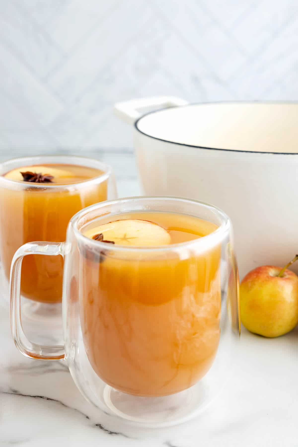 Glasses of wassail in front of a white pot.