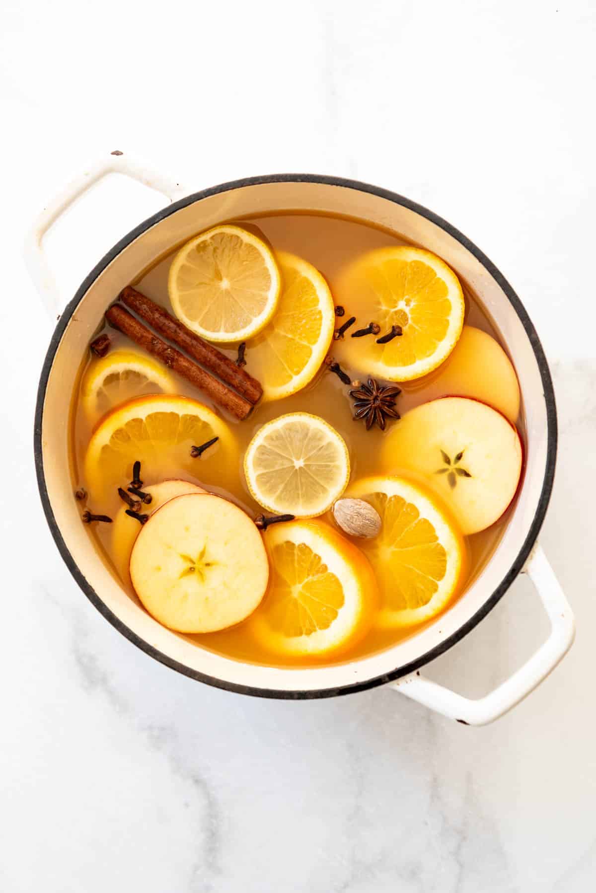 An overhead image of a large pot of wassail with sliced fruit and whole spices.