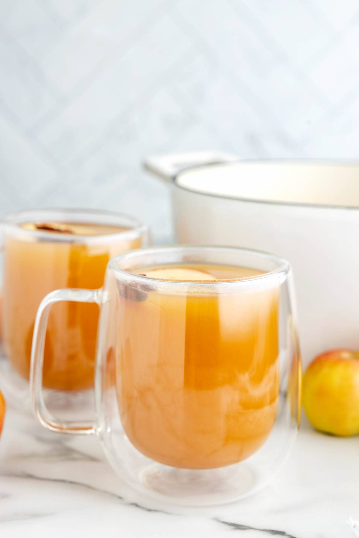A glass mix filled with homemade wassail in front of a white pot.