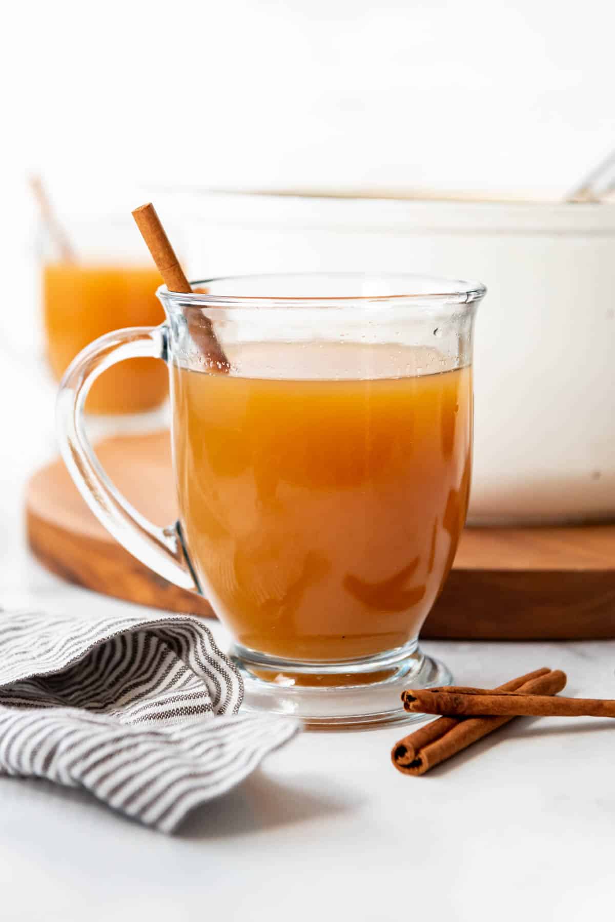 A glass mug filled with wassail and a cinnamon stick.