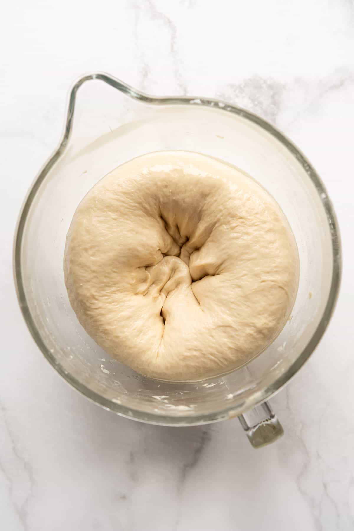 Bread dough that has been punched down in a glass mixing bowl.