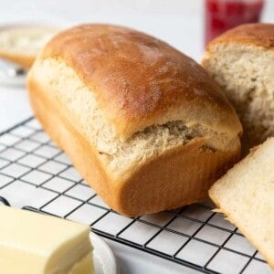 A loaf of fresh homemade Amish white bread on a cooling rack in front of a butter plate with softened butter.