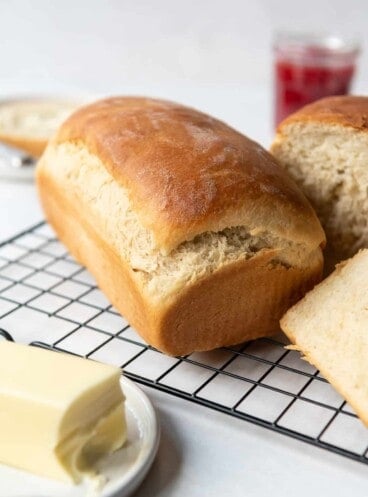 A loaf of fresh homemade Amish white bread on a cooling rack in front of a butter plate with softened butter.