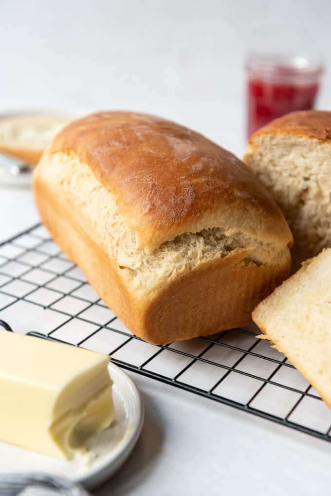 A loaf of fresh homemade Amish white bread on a cooling rack in front of a butter plate with softened butter.