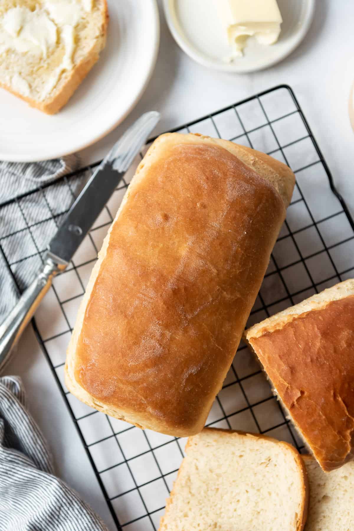 A loaf of homemade Amish white bread next to another sliced loaf and butter knife.