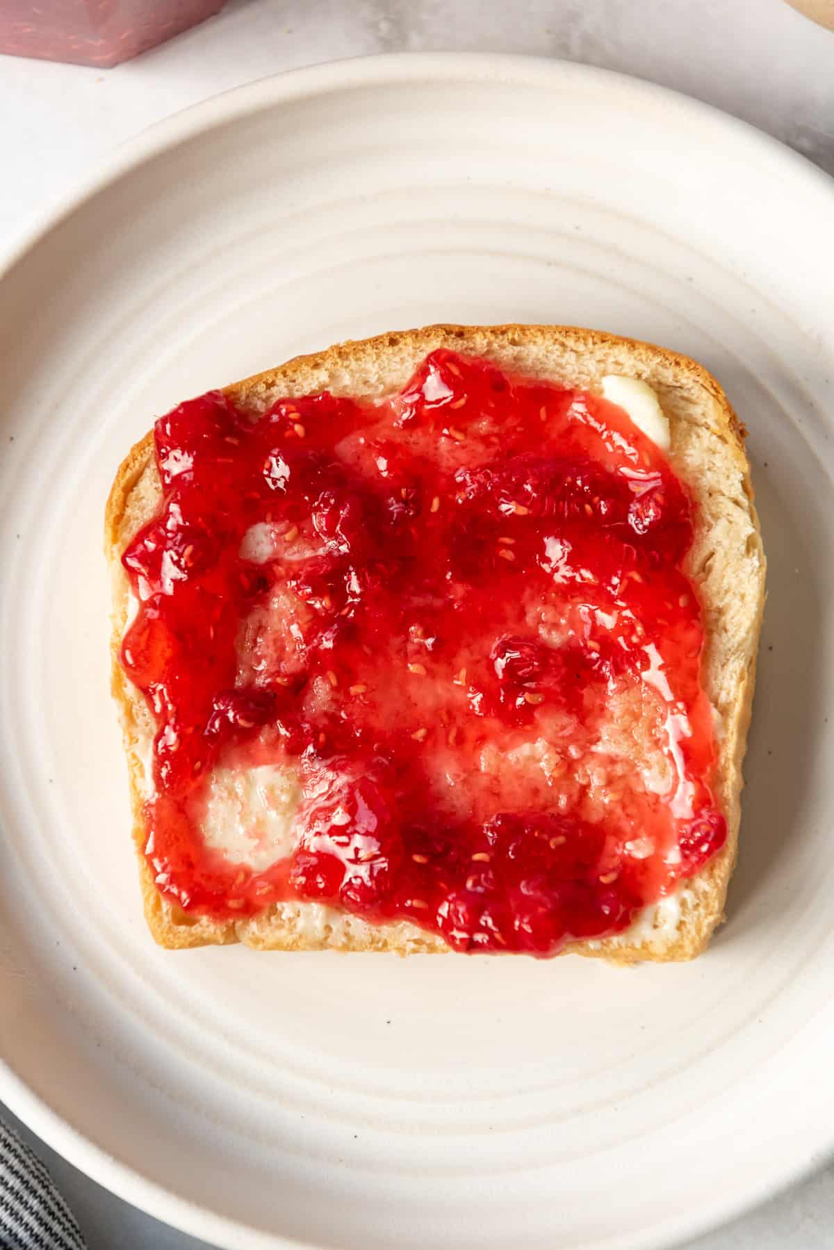 A slice of fresh homemade white bread with raspberry freezer jam spread on top.