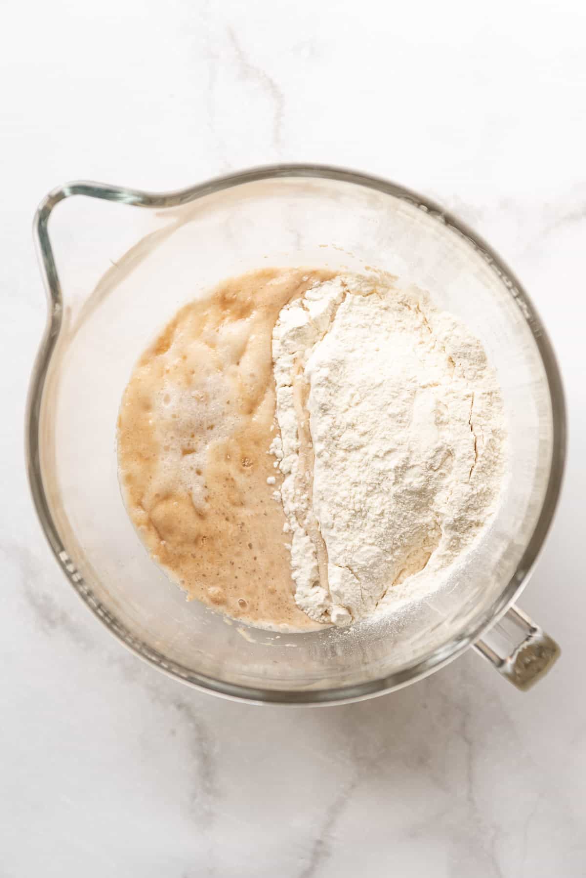 Adding bread flour to proofed yeast in a bowl.