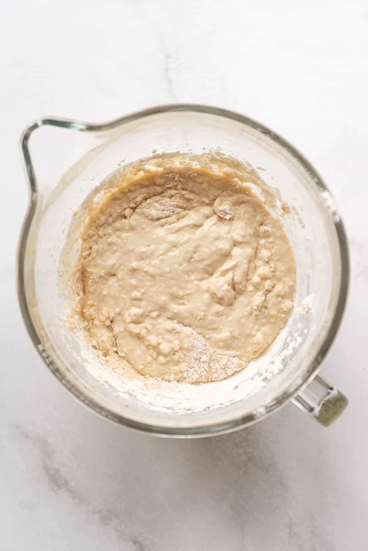 Bread dough that needs more flour added to it in a glass bowl.