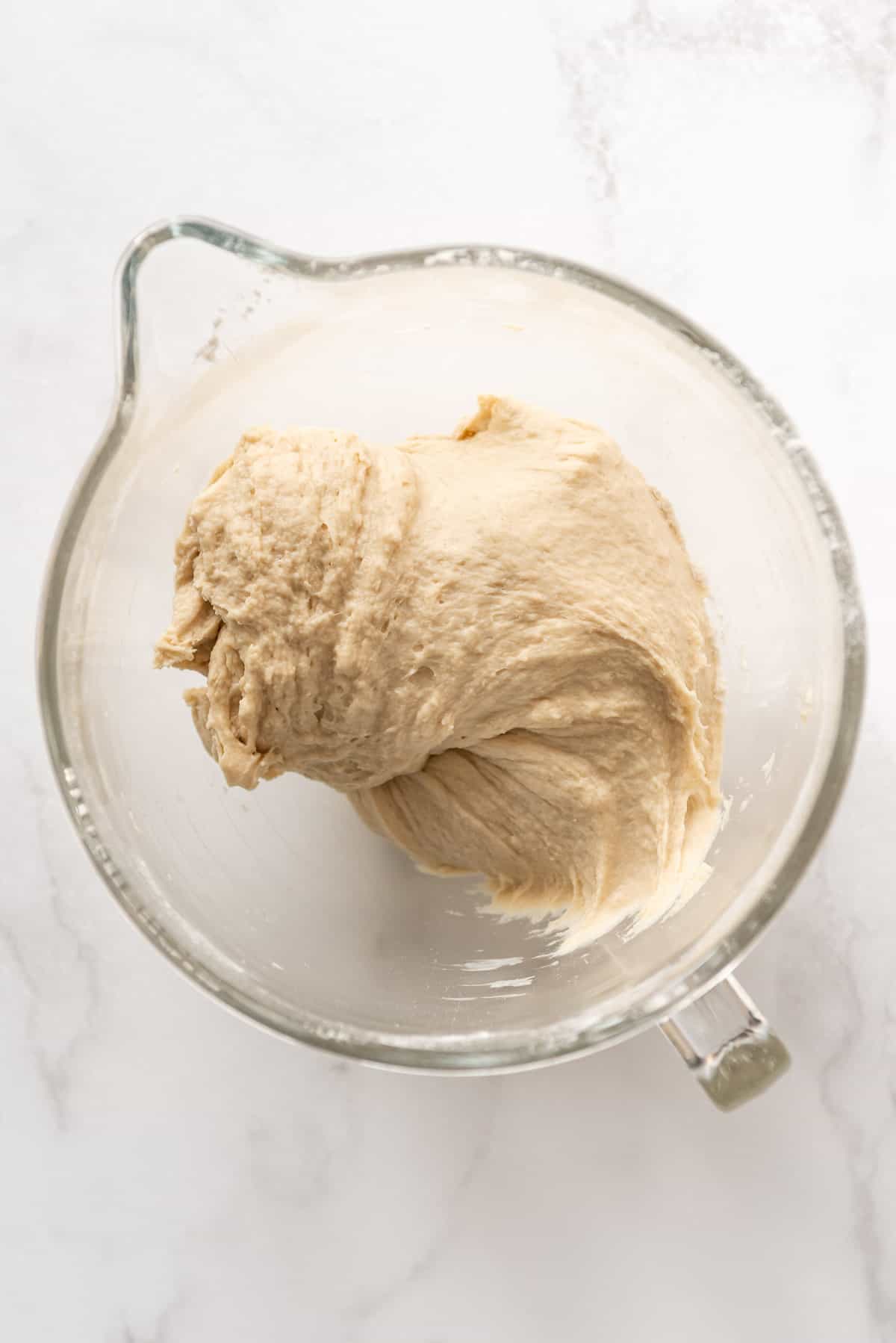 Kneaded bread dough in a glass bowl.