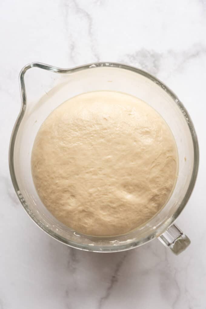 Risen bread dough in a glass mixing bowl.