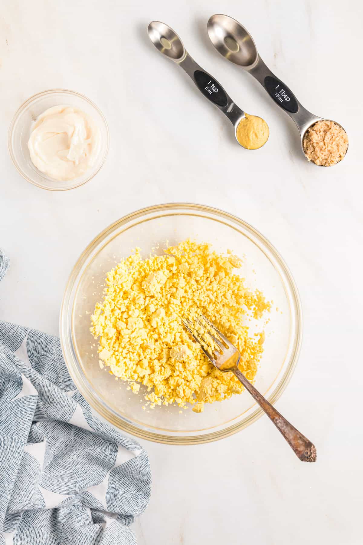 Mashing cooked egg yolks in a bowl with a fork.