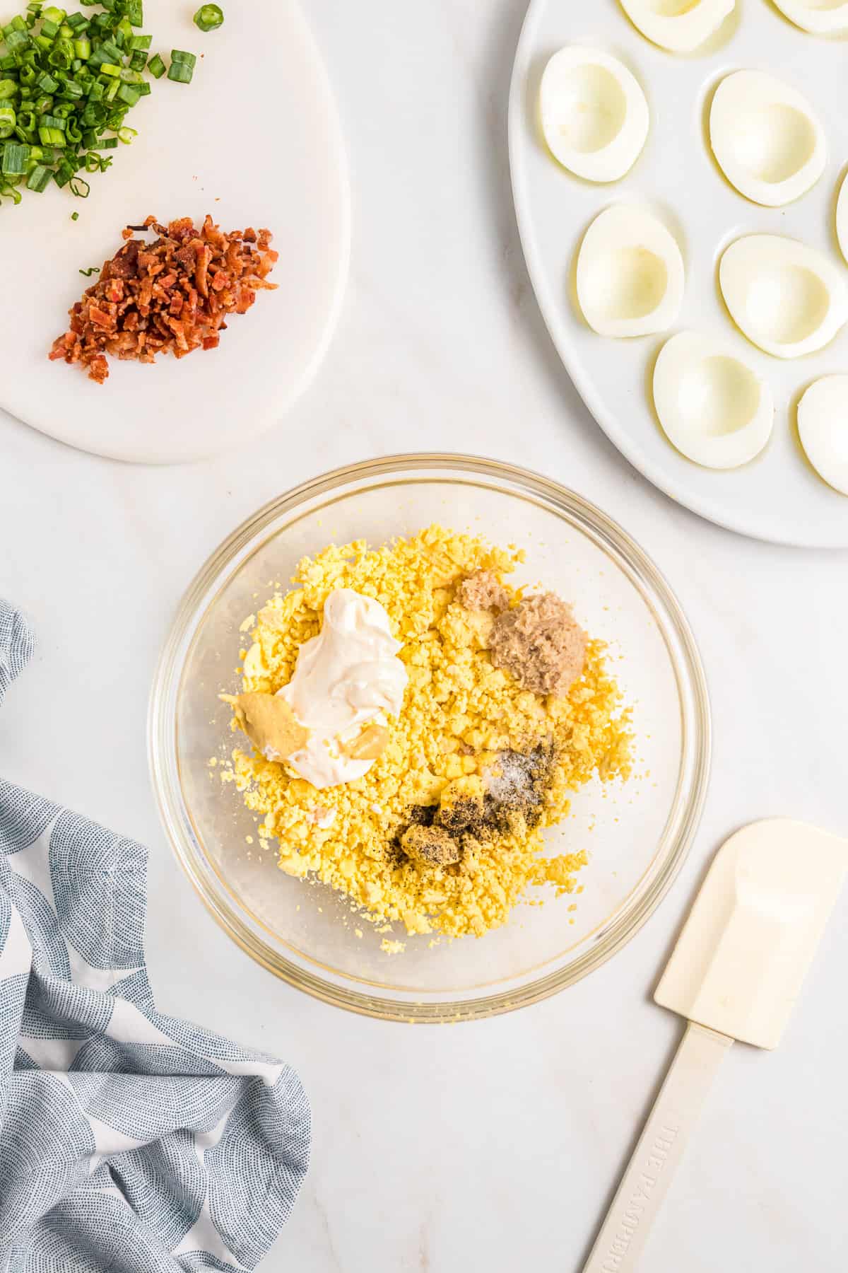 Adding mayonnaise, mustard, horseradish, salt, and spices to egg yolk filling for deviled eggs.