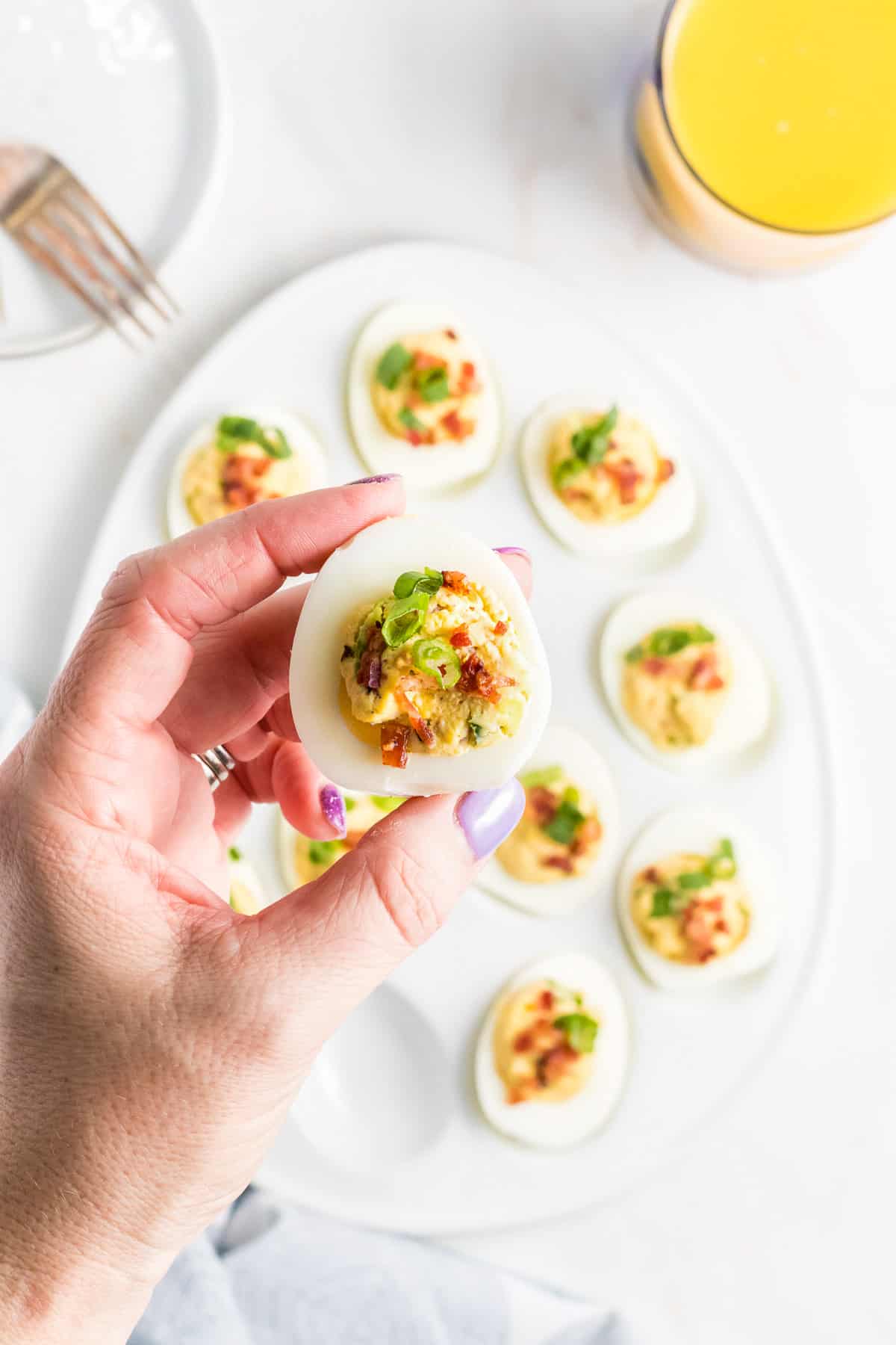 A hand holding up a deviled egg with bacon and green onions.