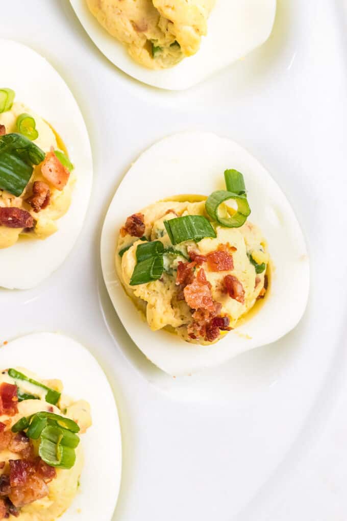 A close image of a deviled egg with a creamy filling and fresh chopped green onions and crispy bacon on top.