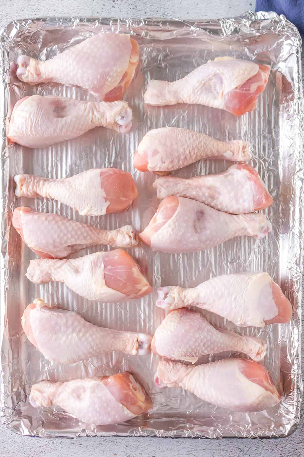 Raw chicken drumsticks on a baking sheet lined with aluminum foil.