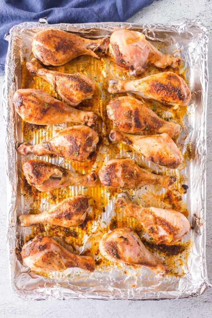 Baked chicken drumsticks on a baking sheet lined with aluminum foil.