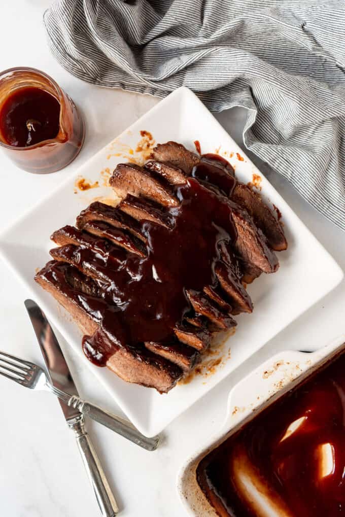 An overhead image of a plated beef brisket that has been sliced against the grain and topped with extra bbq sauce.