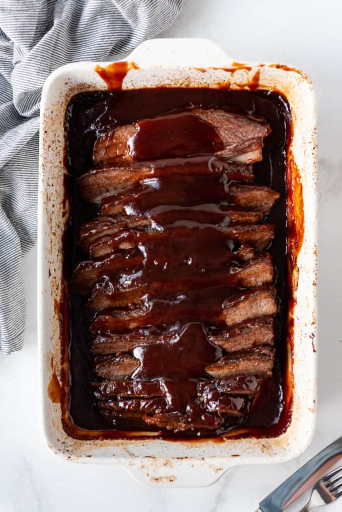 A large white baking dish filled with a sliced brisket slow cooked then covered in bbq sauce.