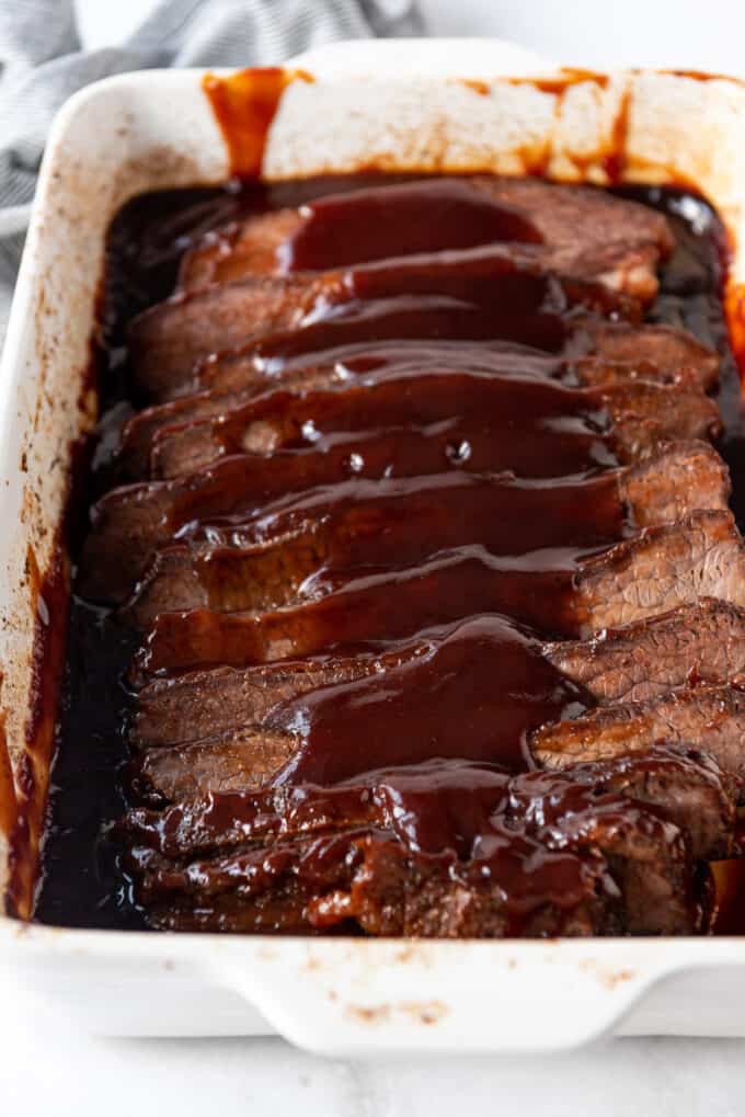 Hickory and brown sugar bbq sauce poured over sliced beef brisket in a white dish.