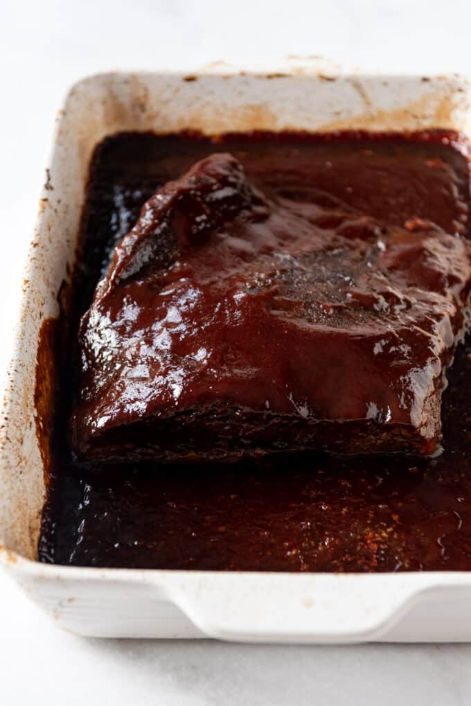 A whole piece of beef brisket in a pan covered in bbq sauce.