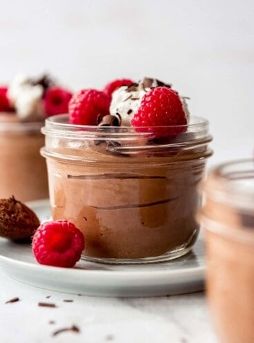 A glass cup filled with chocolate mousse topped with whipped cream and raspberries.