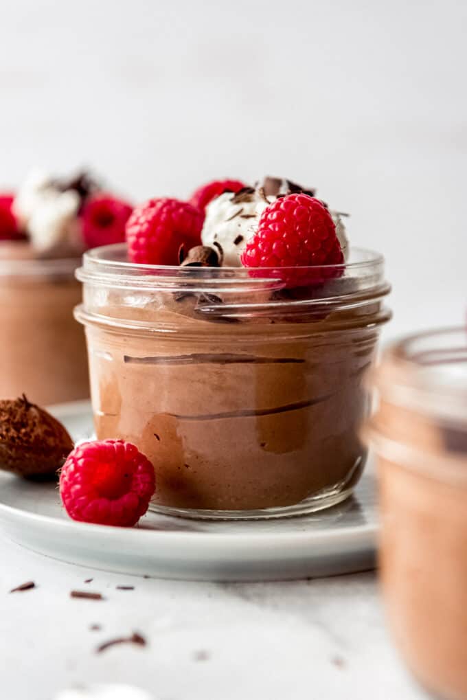 A glass cup filled with chocolate mousse topped with whipped cream and raspberries.