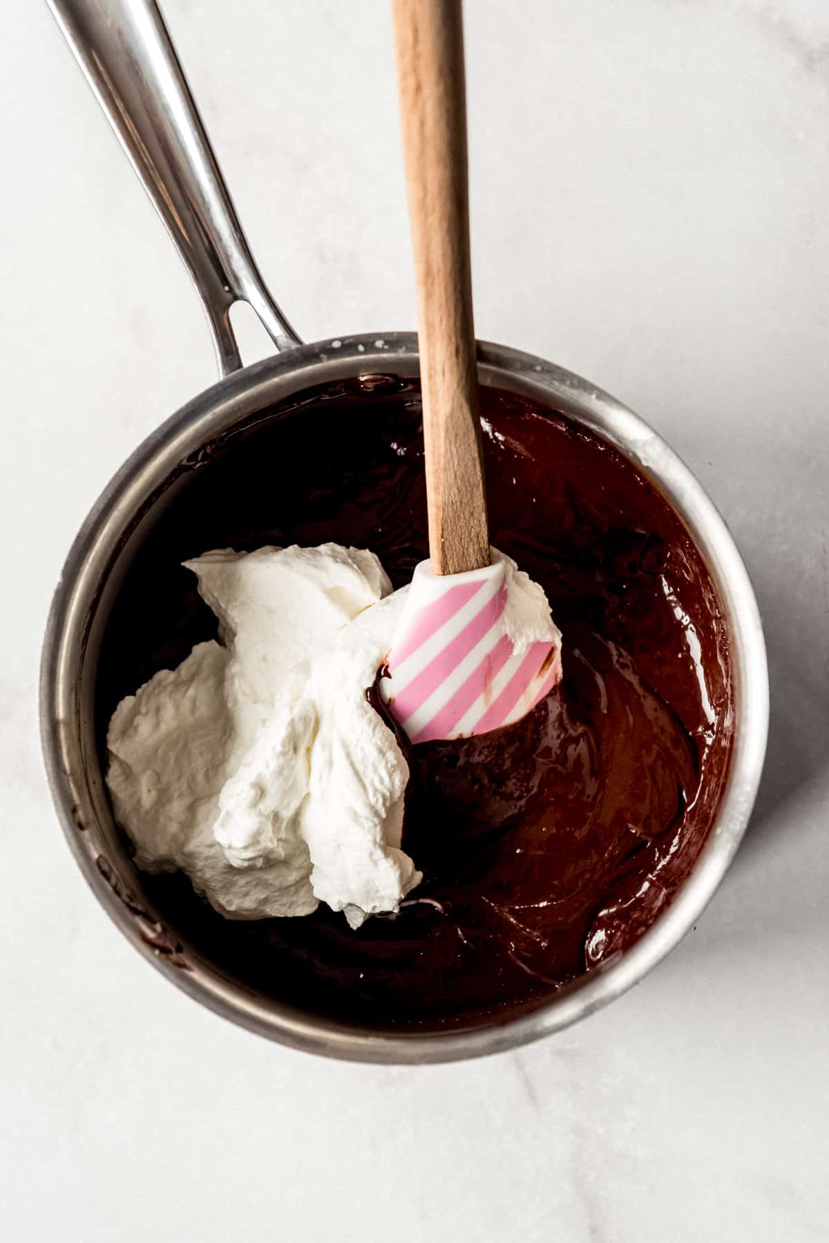 Adding freshly whipped cream to a chocolate custard base in a saucepan.