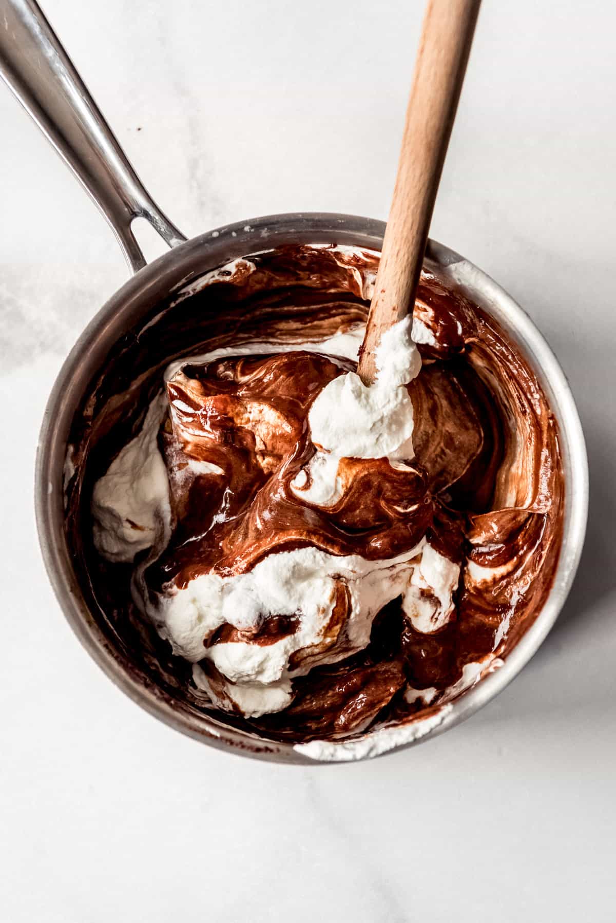 Folding whipped cream into a chocolate custard base in a saucepan.