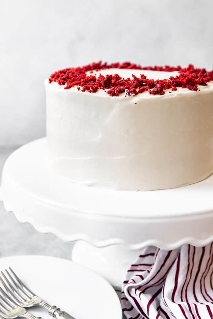 An image of a frosted red velvet cake with cream cheese frosting and red velvet crumbs sprinkled on top.
