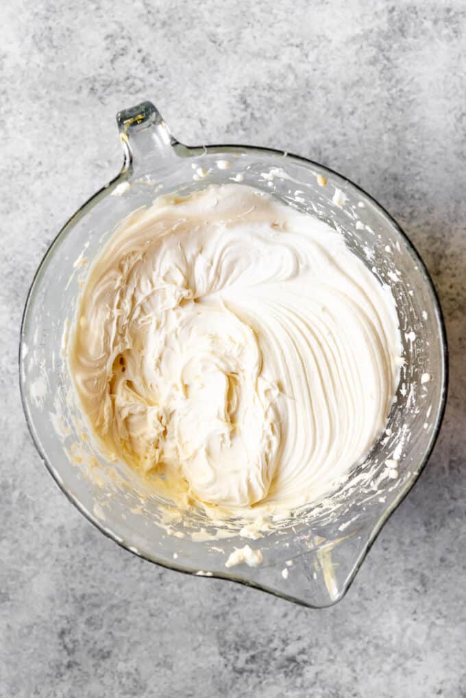 An image of cream cheese frosting that has been mixed in a bowl with a hand mixer.