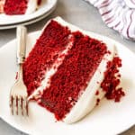 An image of a piece of homemade red velvet cake on a white plate with a fork.