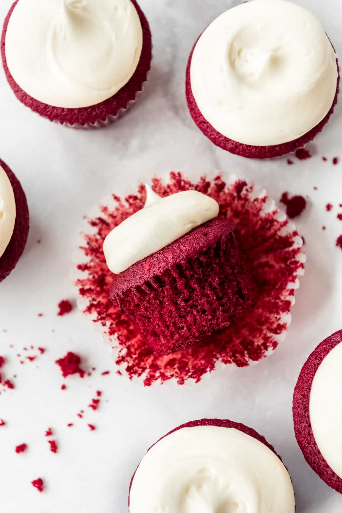 Overhead image of red velvet cupcakes with frosting on marble counter, one cupcake on it's side.