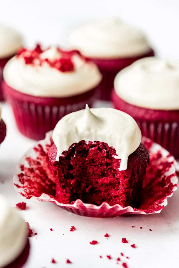 A red velvet cupcake on its wrapper with a bite taken out of it in front of more cupcakes.