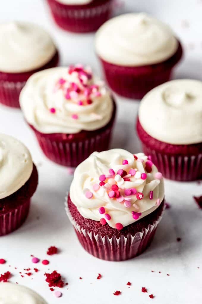 Frosted red velvet cupcakes with cream cheese frosting and Valentine's Day sprinkles on top for decoration.
