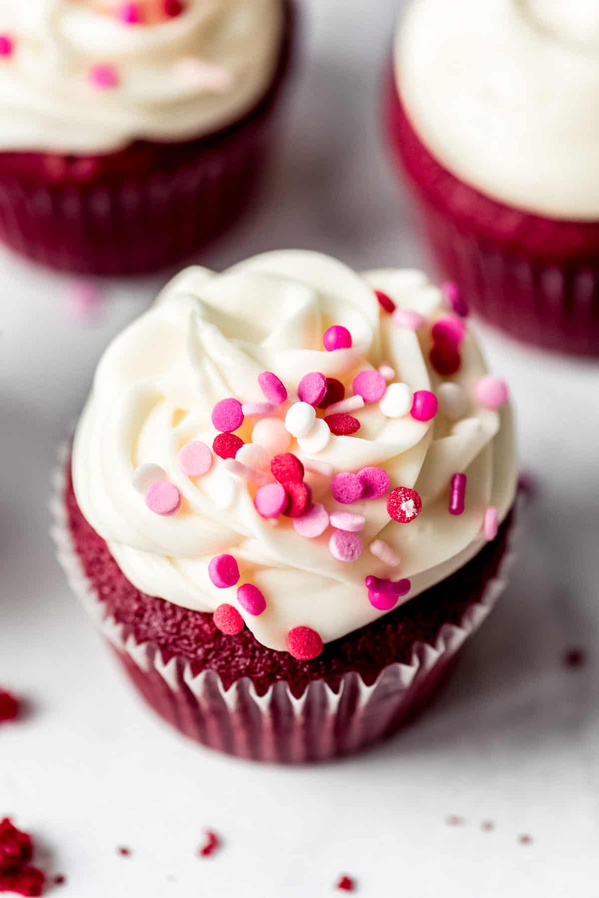 Red velvet cupcake with frosting and pink sprinkles on marble counter.