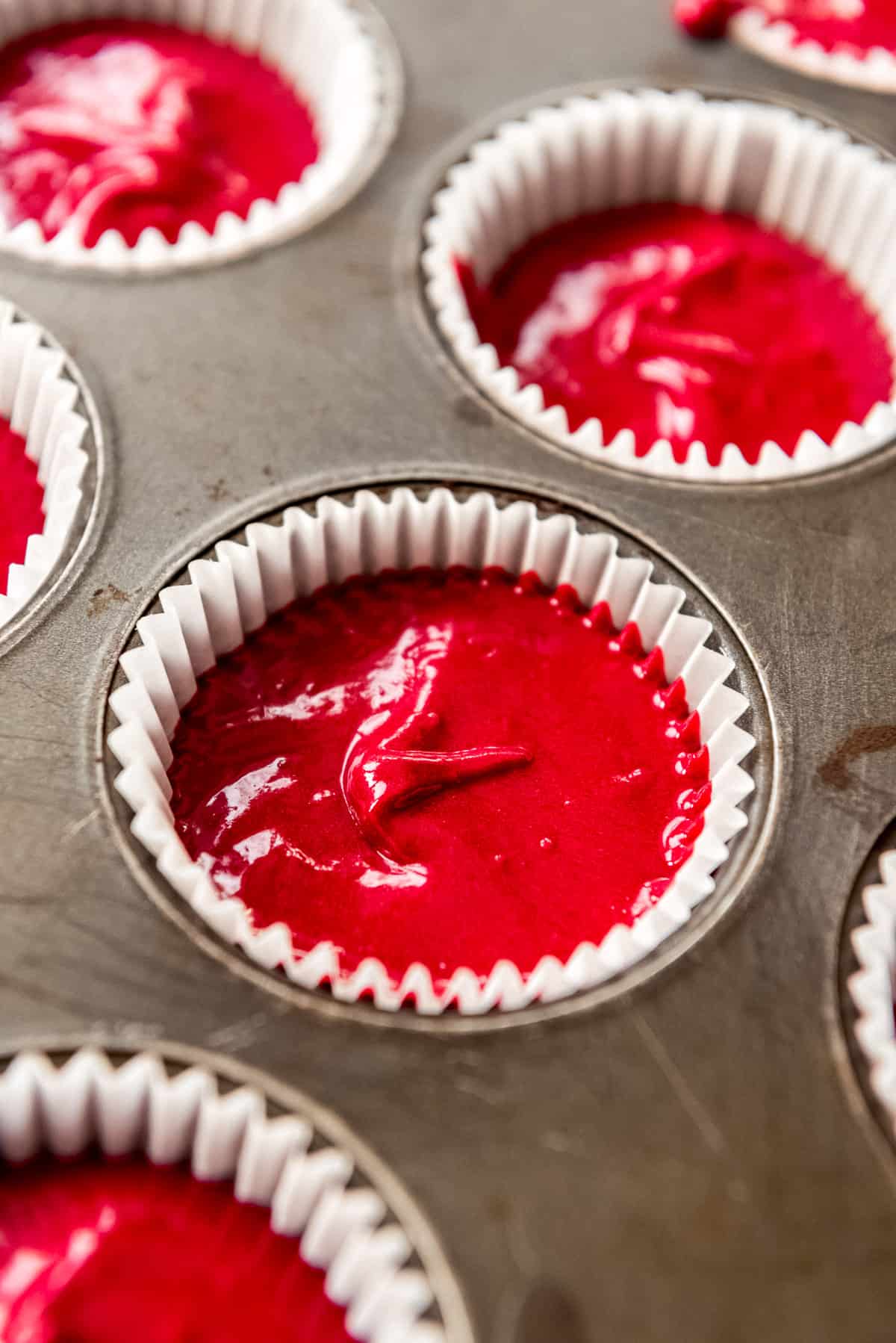 Homemade red velvet cake batter in cupcake liner in tray, ready to bake.