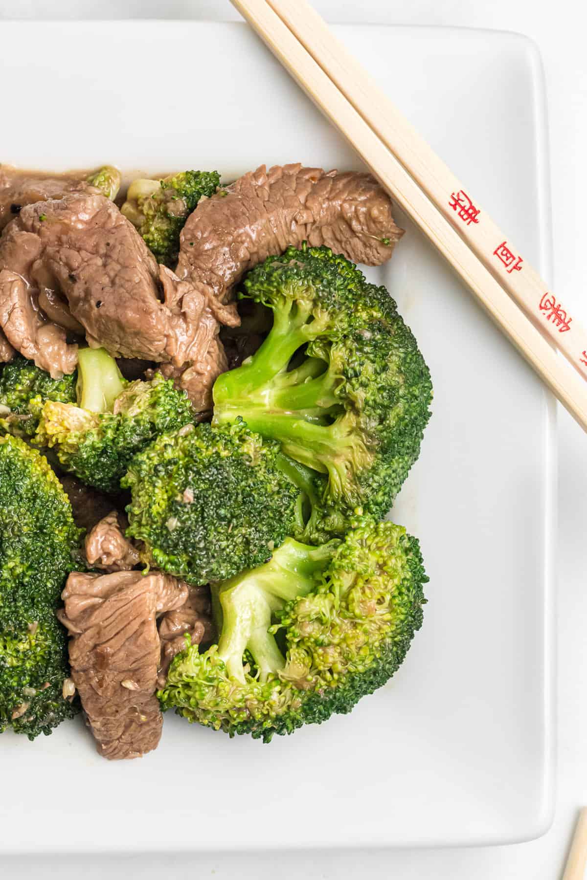 Chinese beef and broccoli on a white plate with chopsticks.