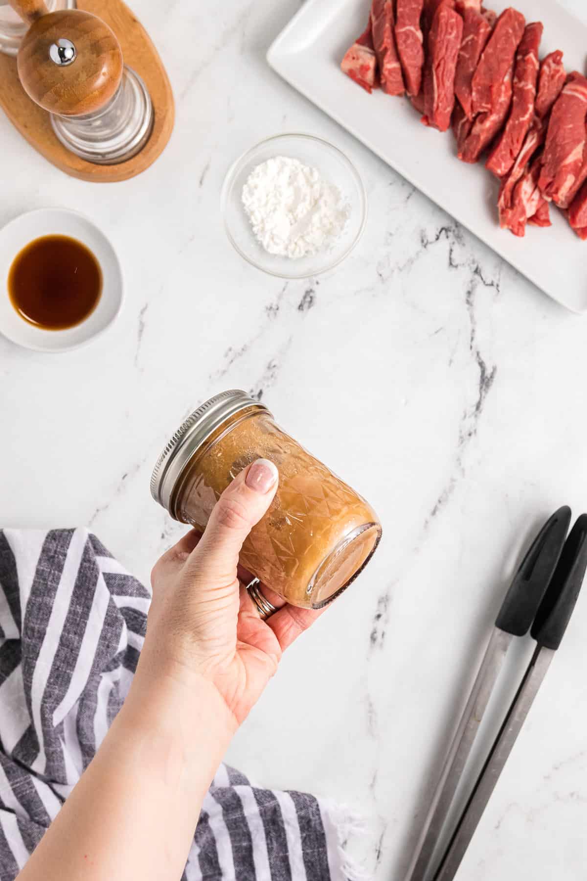 A hand shaking a jar of sauce to combine ingredients.