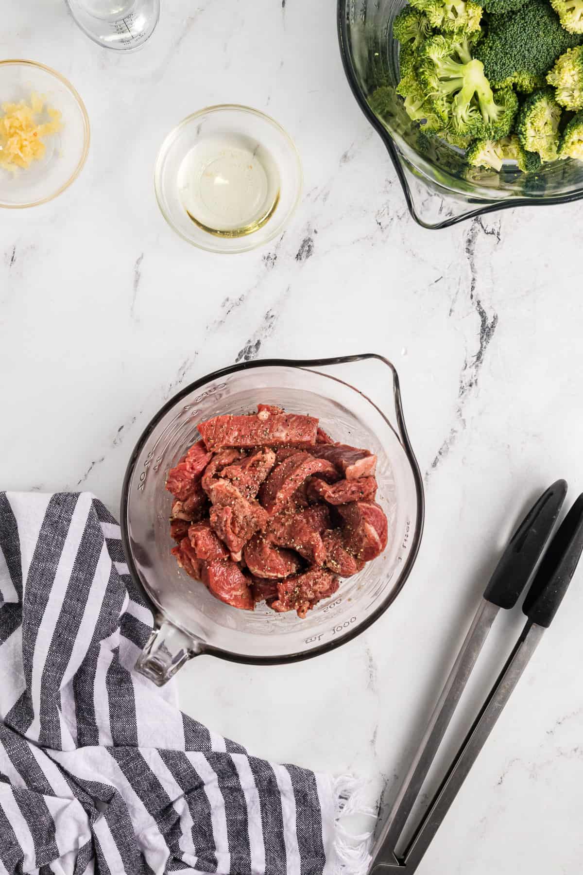 Strips of beef tossed with cornstarch in a glass bowl.