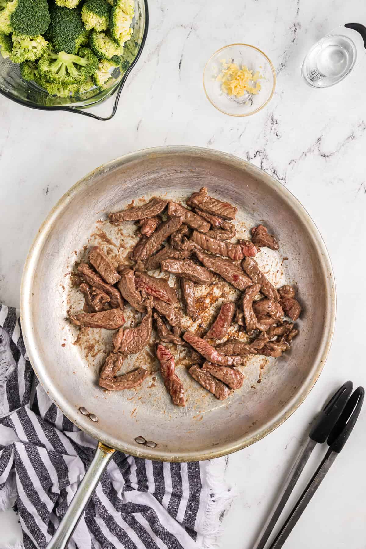 Searing strips of beef in a large pan.