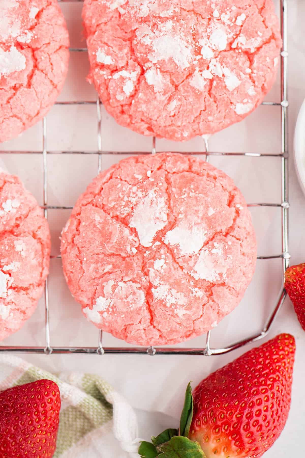Strawberry crinkle cookies on a wire rack next to strawberries.