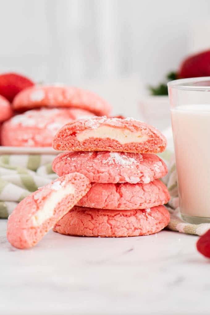Stacked strawberry cheesecake cookies next to a glass of milk.