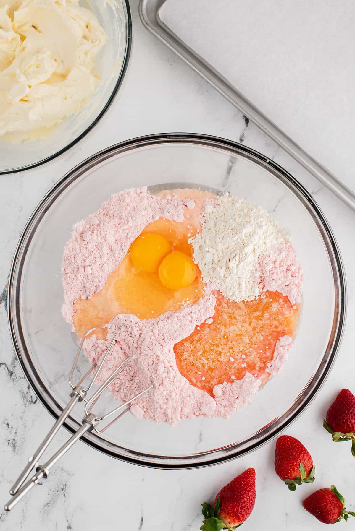 Adding eggs and melted butter to strawberry cake mix in a glass bowl.