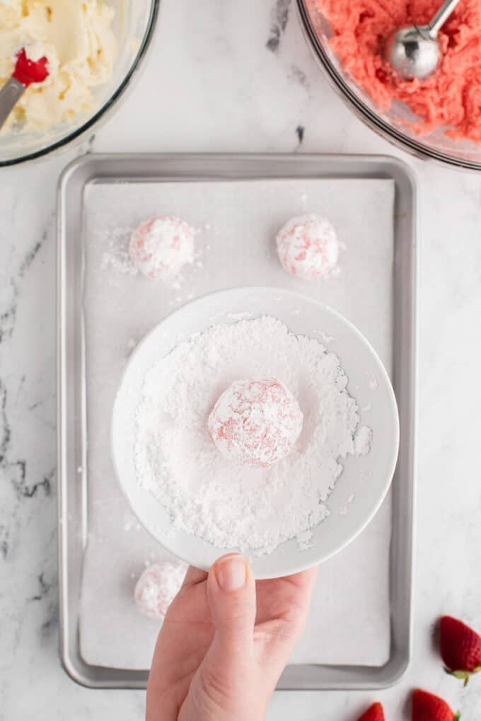 Rolling a ball of strawberry cake mix cookie dough in a bowl of powdered sugar.