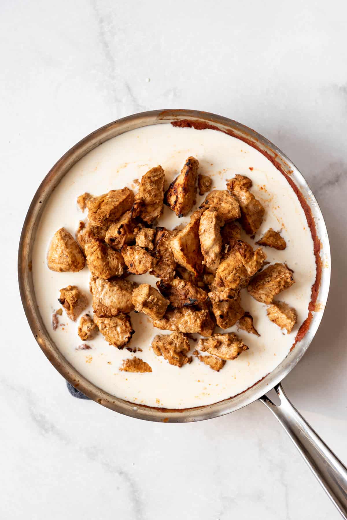 Adding cooked chicken into a spiced tomato sauce with heavy cream.