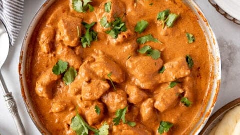 A large skillet of chicken tikka masala next to a bowl of rice and a plate of garlic naan.